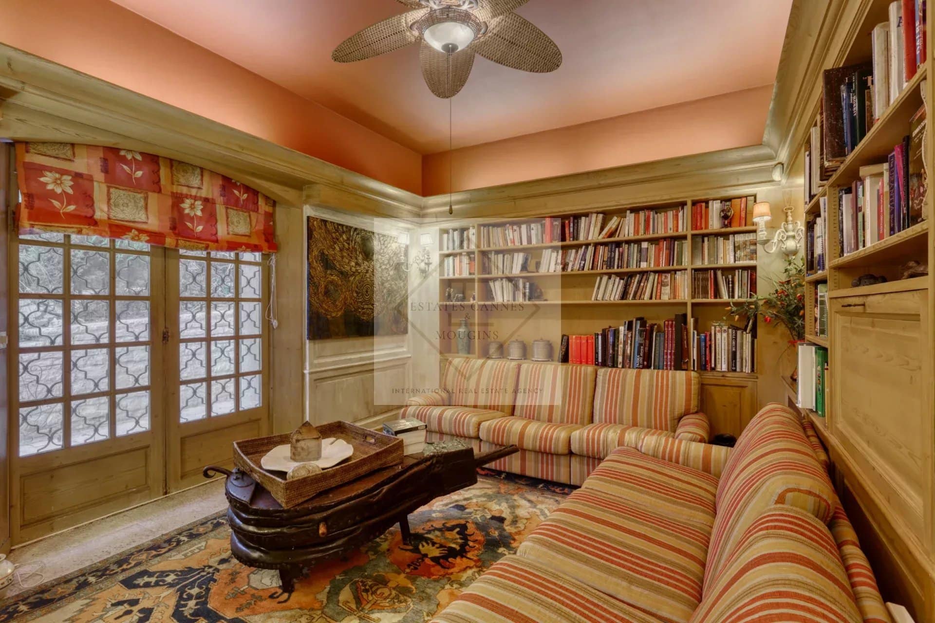 Intérieur d'une villa à Mougins avec salon, bibliothèque et fenêtres en bois.