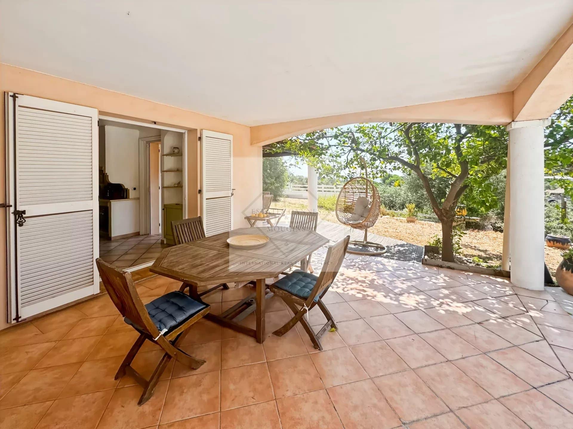 Terrace of a villa in Antibes with wooden table and chairs, surrounded by greenery.