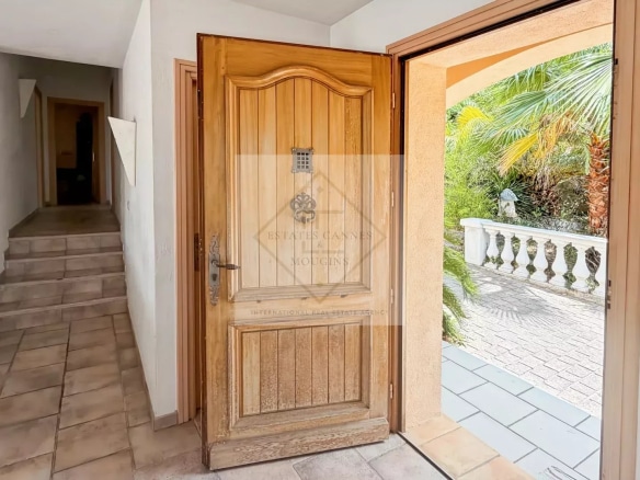 Entrance to a villa with a wooden door and a view of a tropical garden in Antibes.