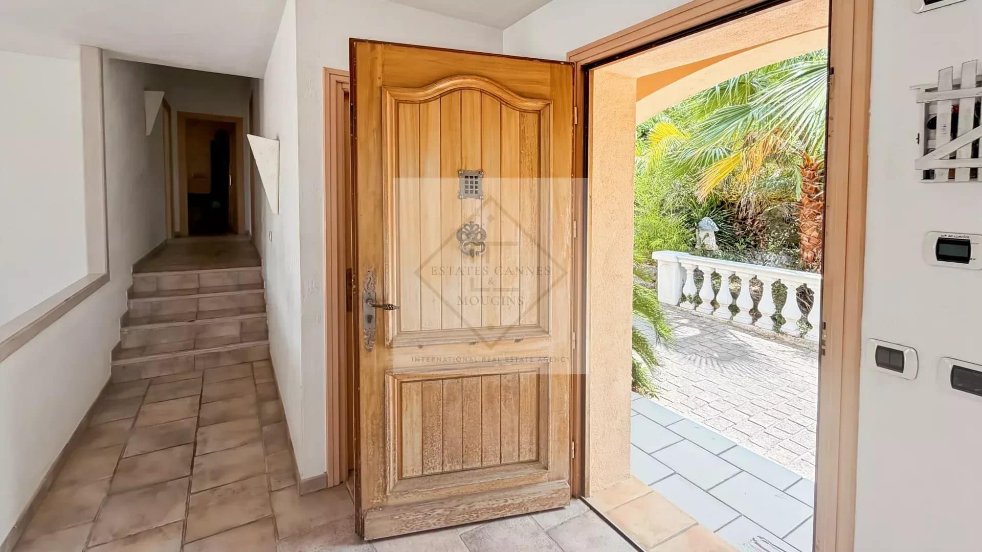 Entrance to a villa with a wooden door and a view of a tropical garden in Antibes.