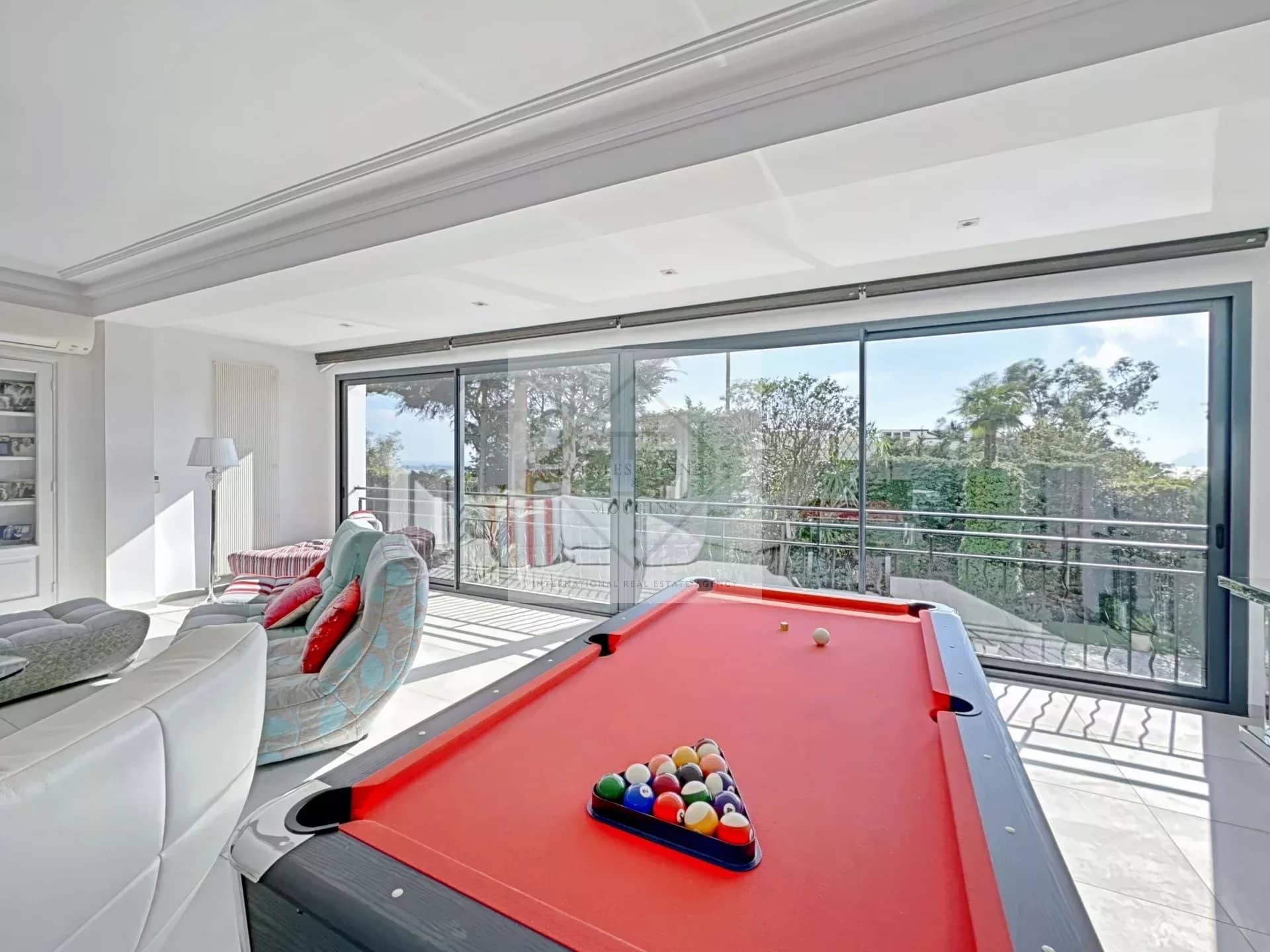 Interior of a luxury villa in Cannes with a pool table and large windows overlooking the garden.