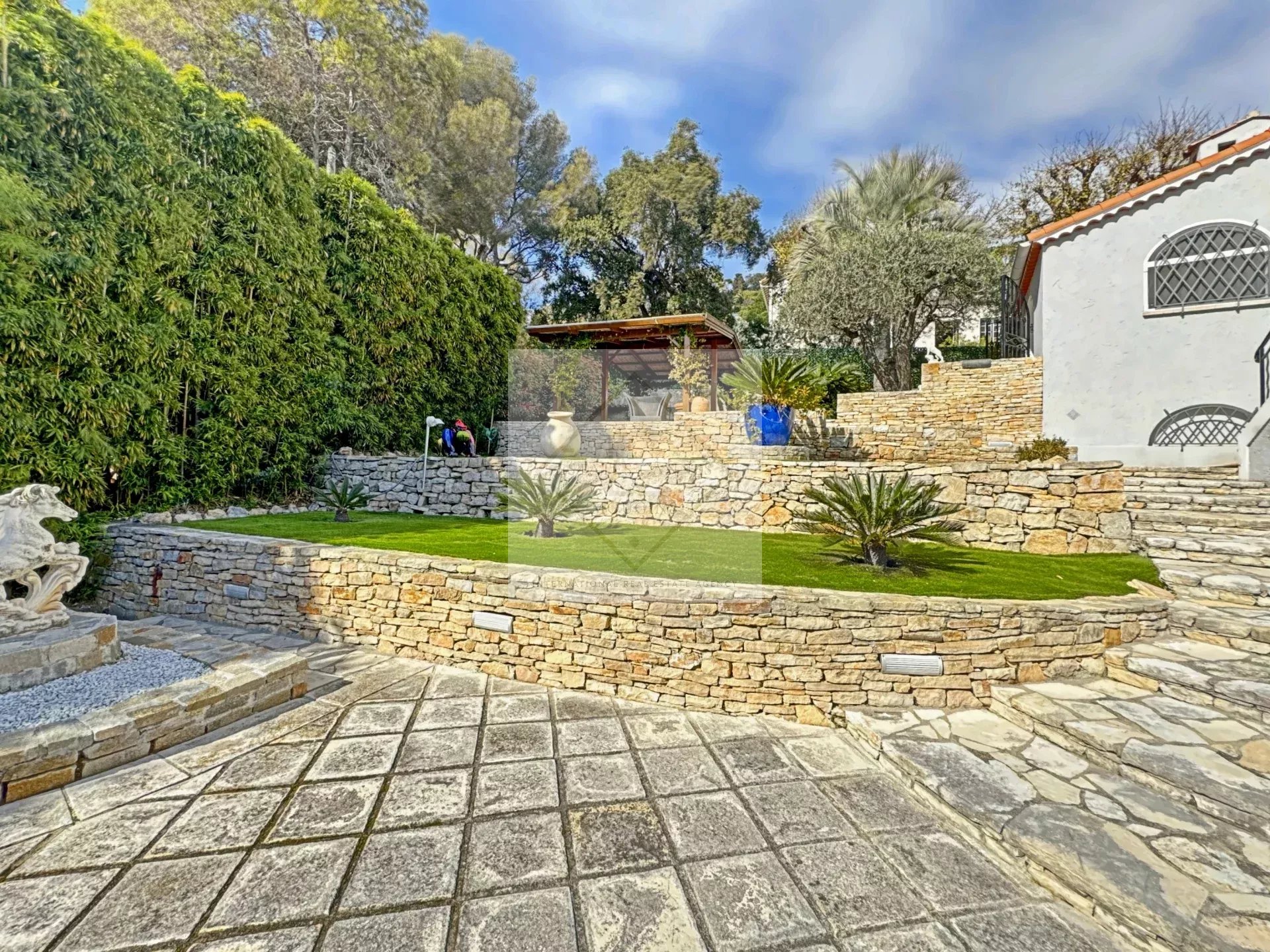 Garden of a luxury villa in Cannes with stone walls and plants.