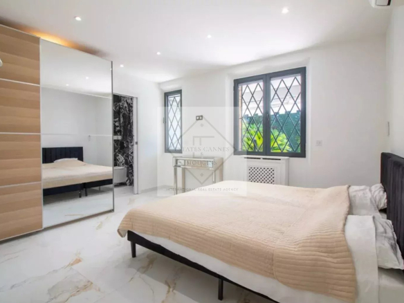 Chambre moderne et lumineuse d'une villa à vendre à Cannes, avec un lit et un grand miroir.