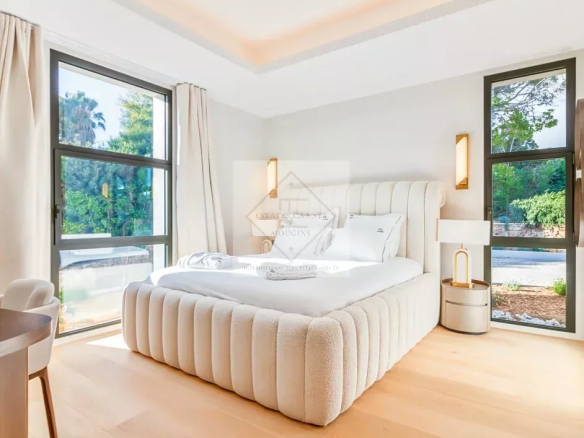 Room in a contemporary villa in Super Cannes, with bed and windows overlooking a garden.