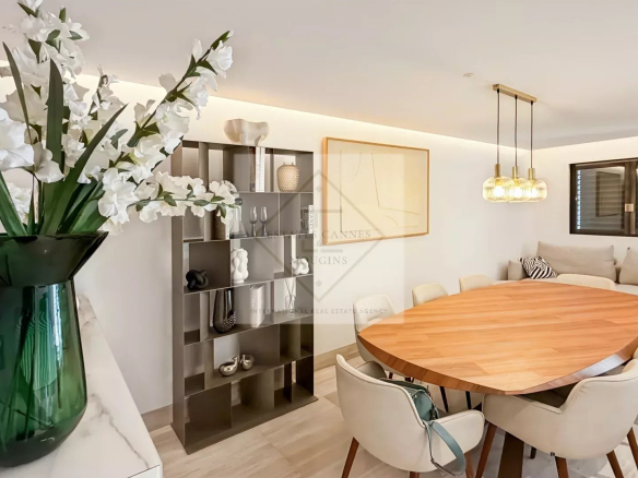 Interior of a modern apartment with a large round table and chairs, decorated with flowers and designer objects.