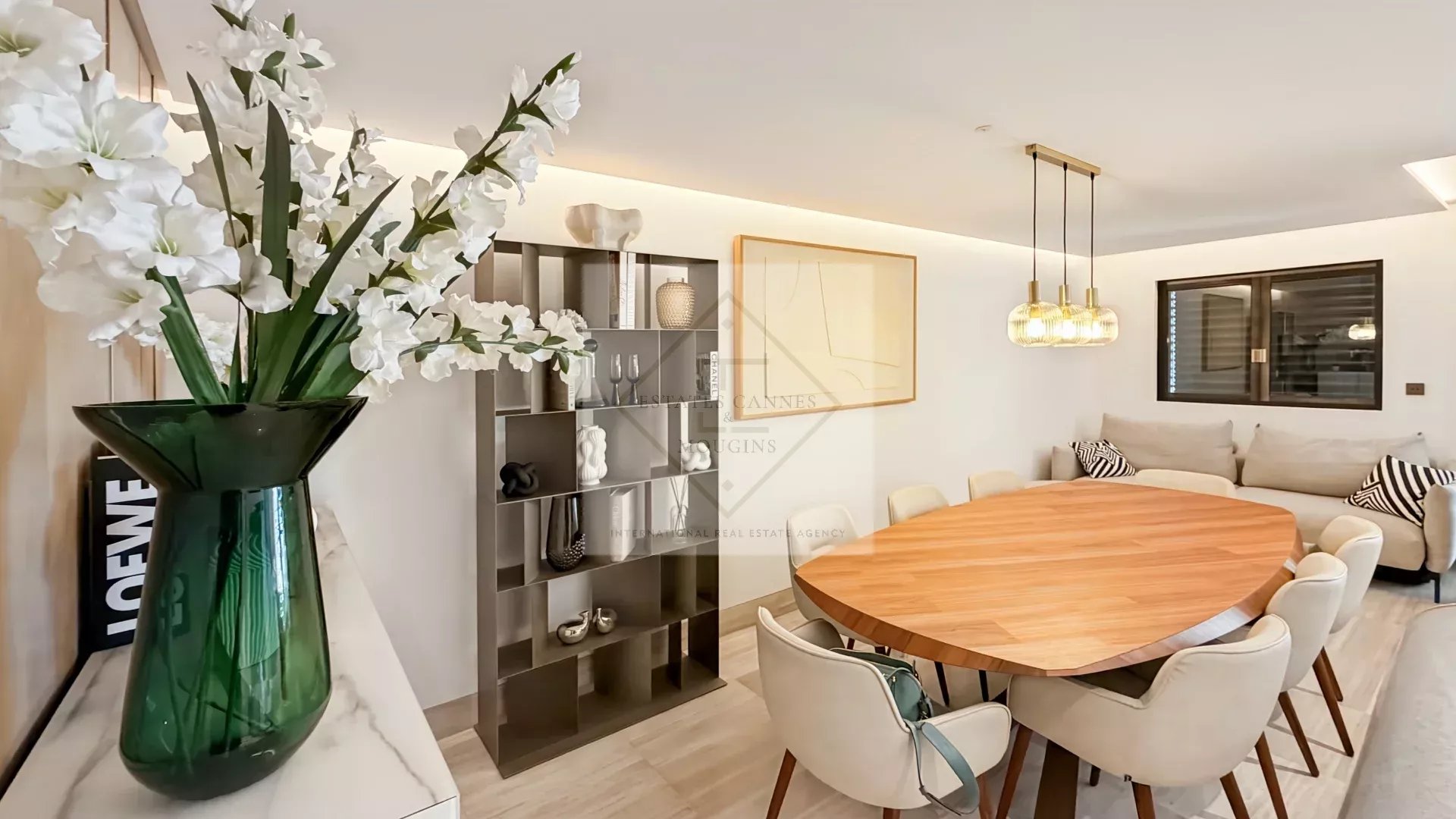Interior of a modern apartment with a large round table and chairs, decorated with flowers and designer objects.