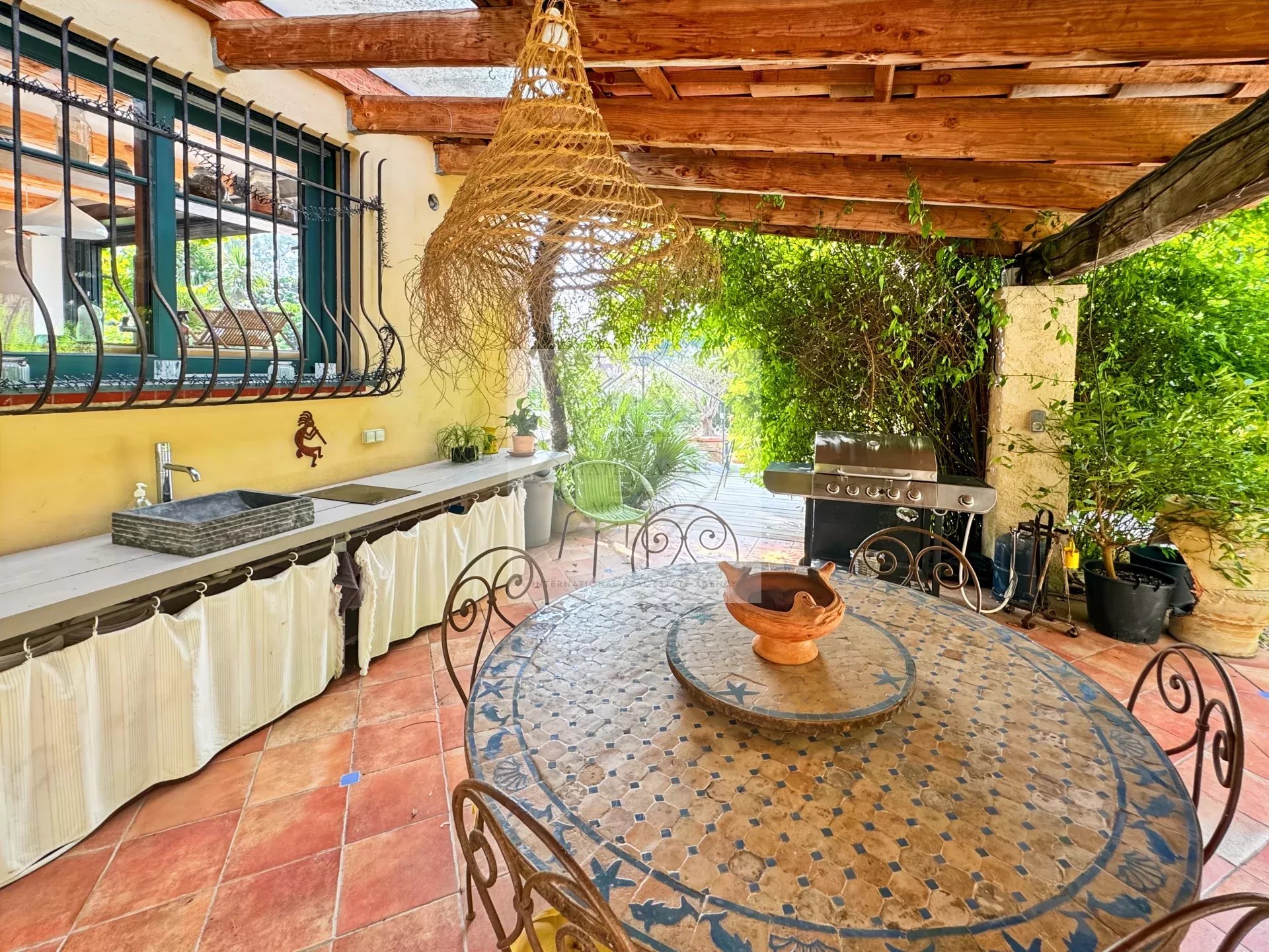 Terrace of the residence in Mougins Outdoor terrace with mosaic table and barbecue, surrounded by greenery.