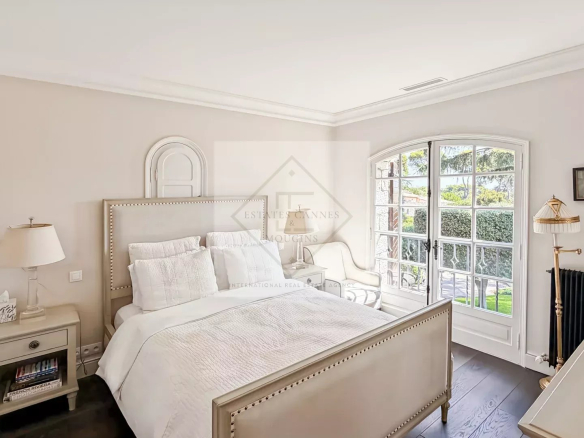Chambre d'une maison en pierre rénovée à Antibes, avec lit élégant et fenêtres offrant une vue sur l'extérieur.