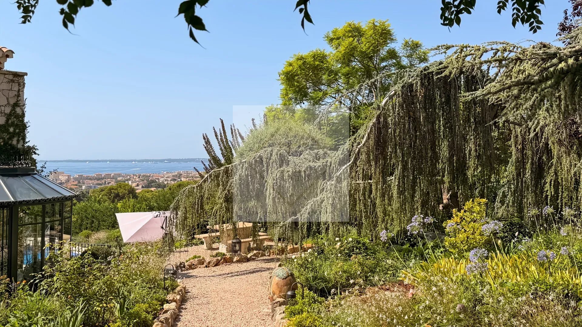 Jardin d’une maison rénovée à Antibes Jardin d'une maison en pierre avec vue sur la mer à Antibes, arbres et plantes luxuriantes.