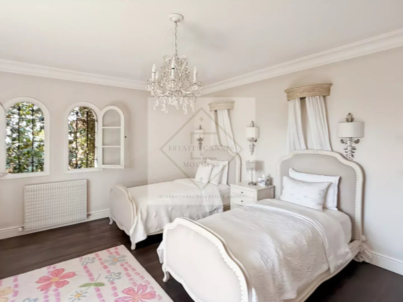 Chambre élégante avec deux lits, décorée dans des tons clairs et un lustre, à Antibes.
