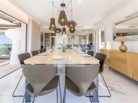 Modern dining room with wooden table and designer chairs, view of the outside, villa in Mougins.