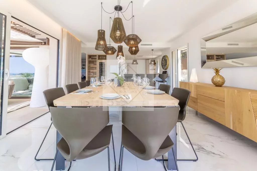 Dining room of a modern villa in Mougins Modern dining room with wooden table and designer chairs, view of the outside, villa in Mougins.