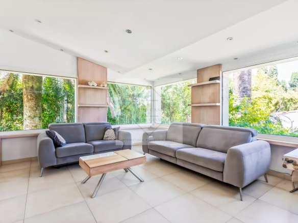 Intérieur d'une villa provençale avec canapés gris et grandes fenêtres donnant sur un jardin.