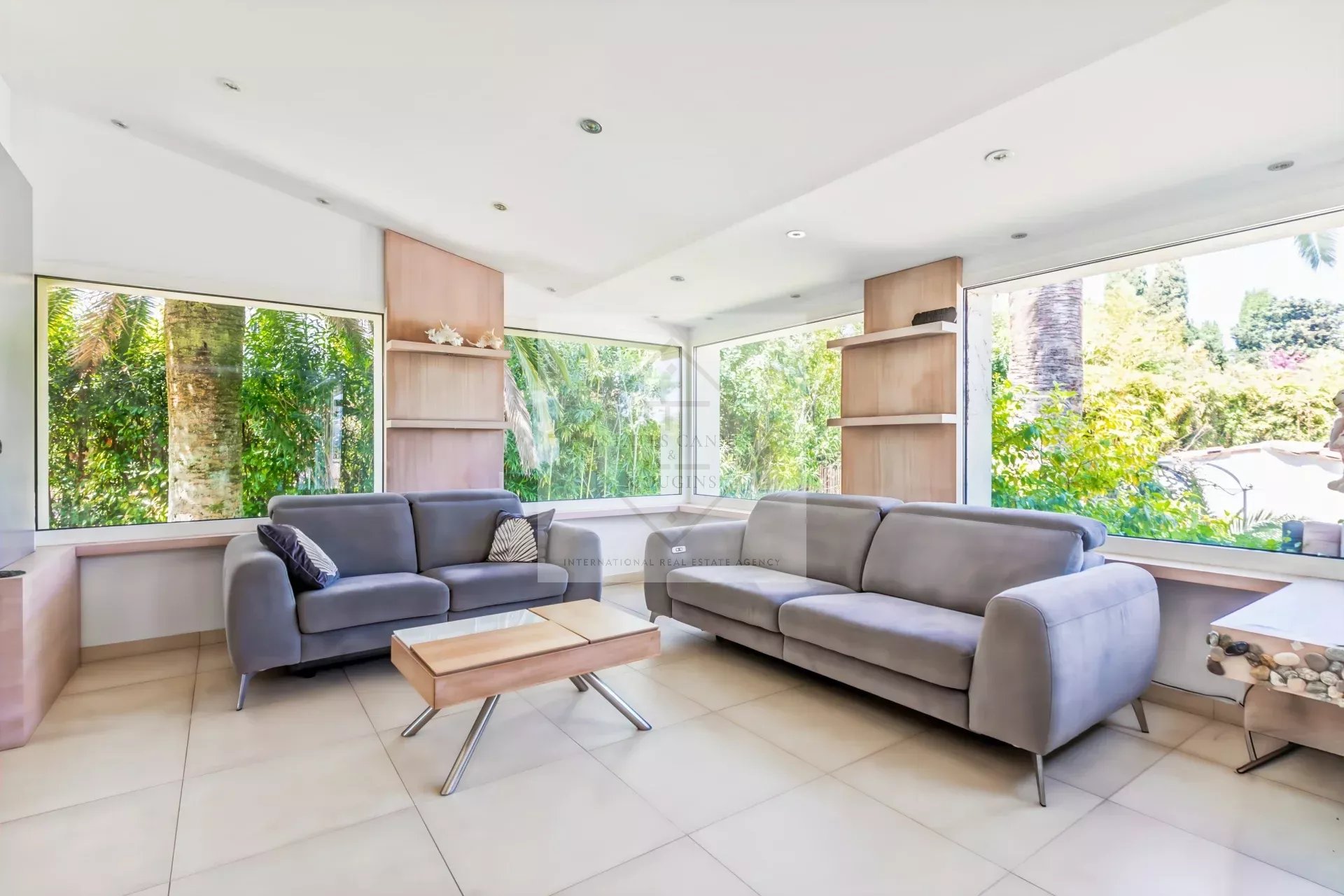 Intérieur d’une villa à Mougins Intérieur d'une villa provençale avec canapés gris et grandes fenêtres donnant sur un jardin.