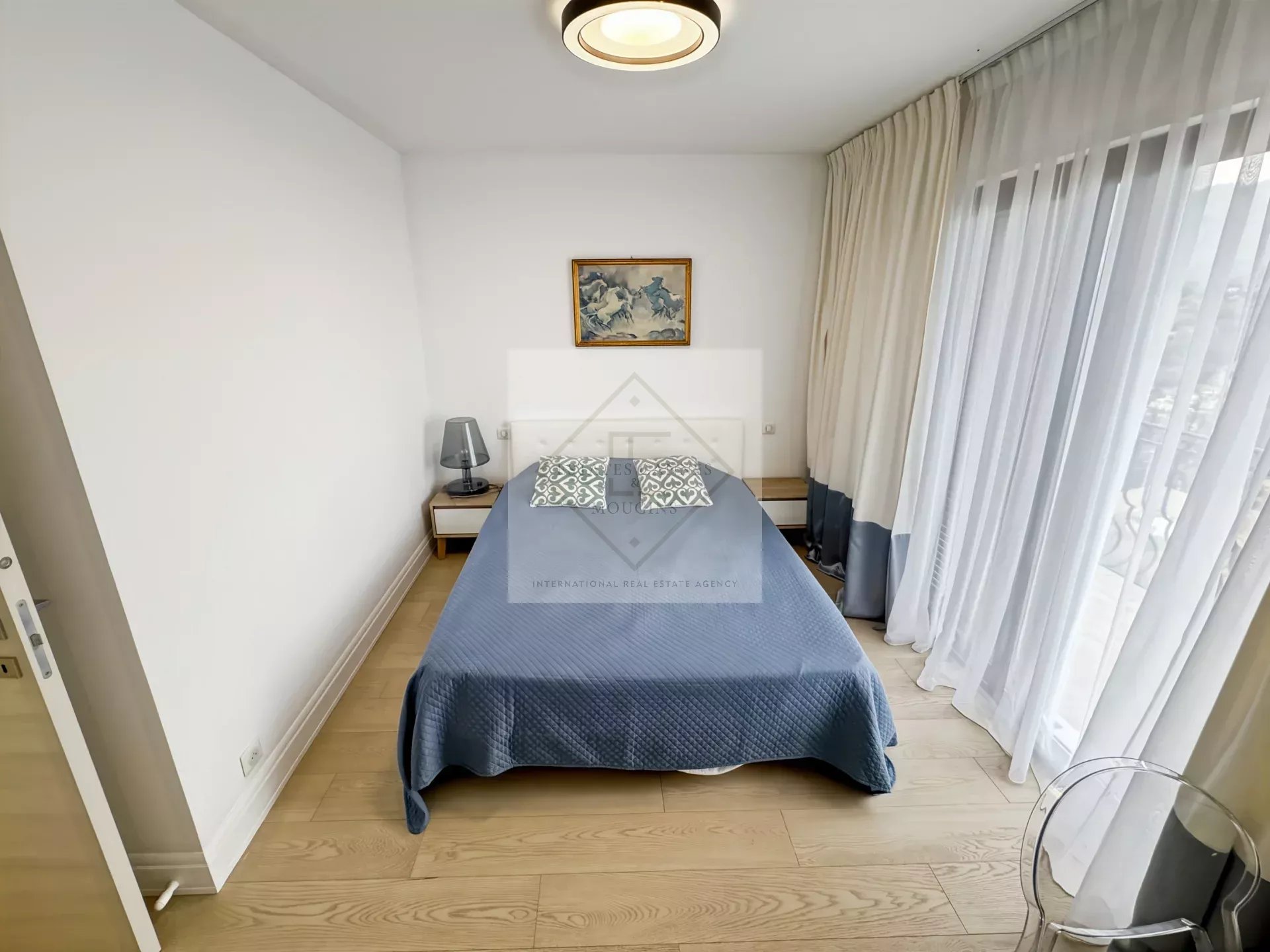 Chambre d'une villa provençale avec lit, décoration simple et fenêtres avec rideaux.