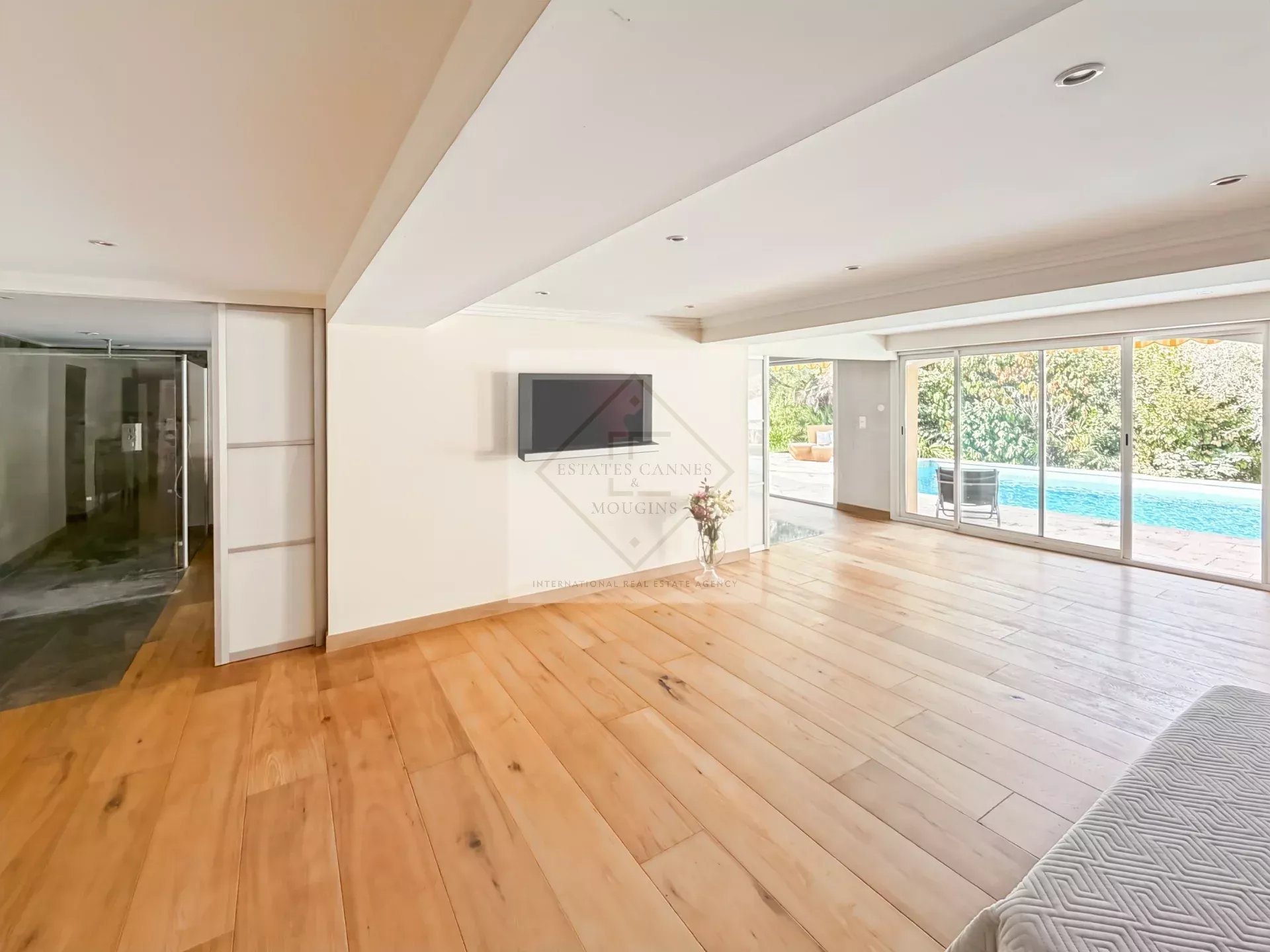 Intérieur d'une villa spacieuse avec un sol en bois et une grande baie vitrée donnant sur la piscine.