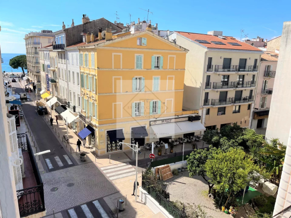 Street view in Cannes with a colorful building and outdoor restaurants.