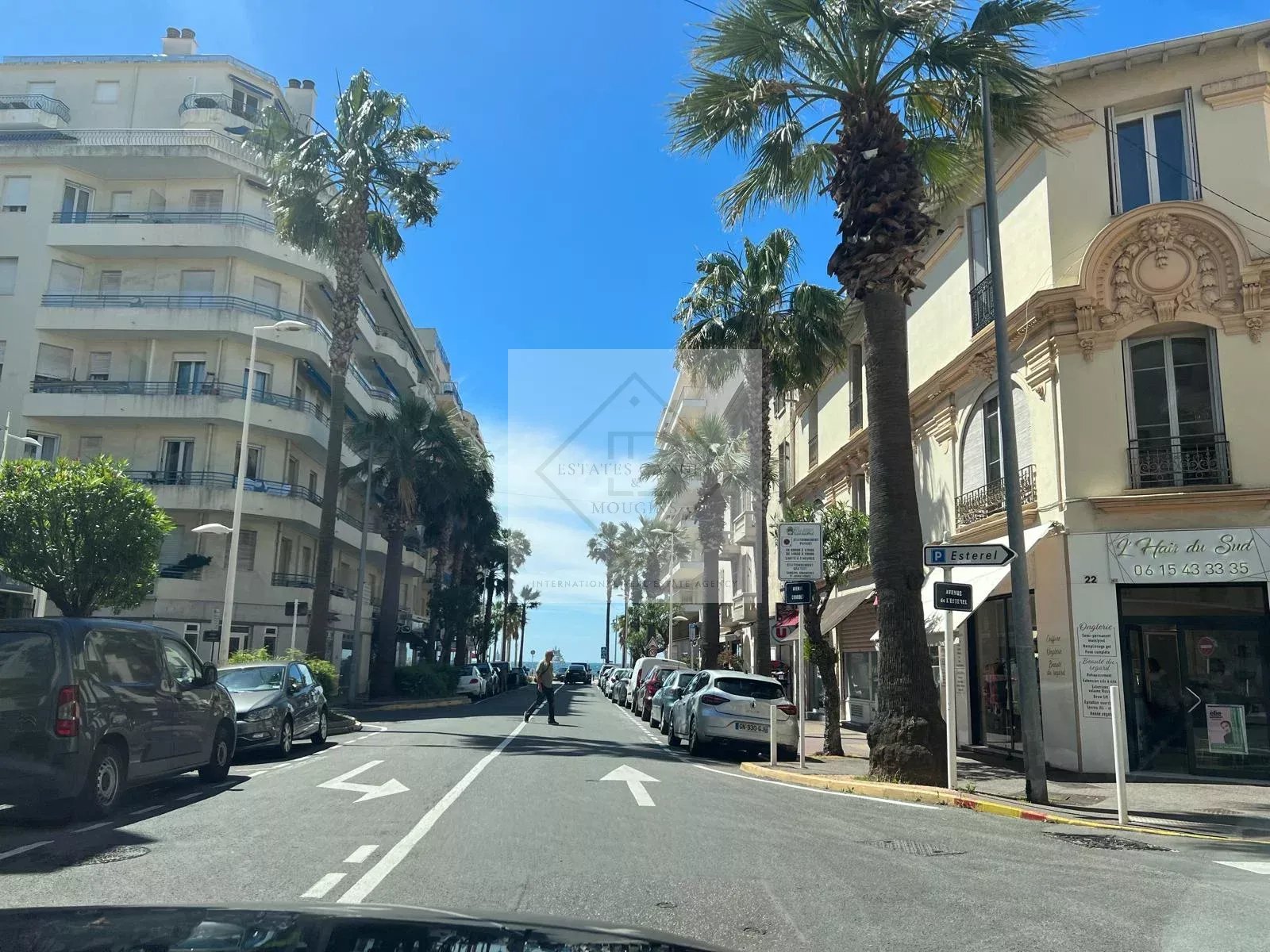 Vue d'une rue à Juan-les-Pins avec palmiers et bâtiments, menant à la plage.
