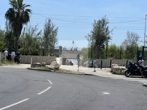 Accès à la plage depuis une rue à Juan-les-Pins, avec des palmiers et des personnes se dirigeant vers la mer.