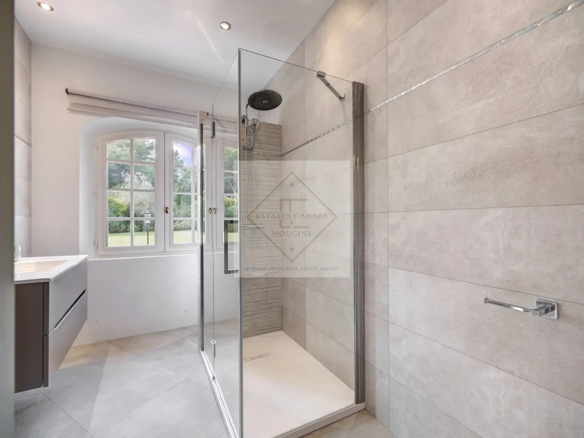 Salle de bain de villa à Mougins Salle de bain moderne avec douche à l'italienne et fenêtre donnant sur le jardin.