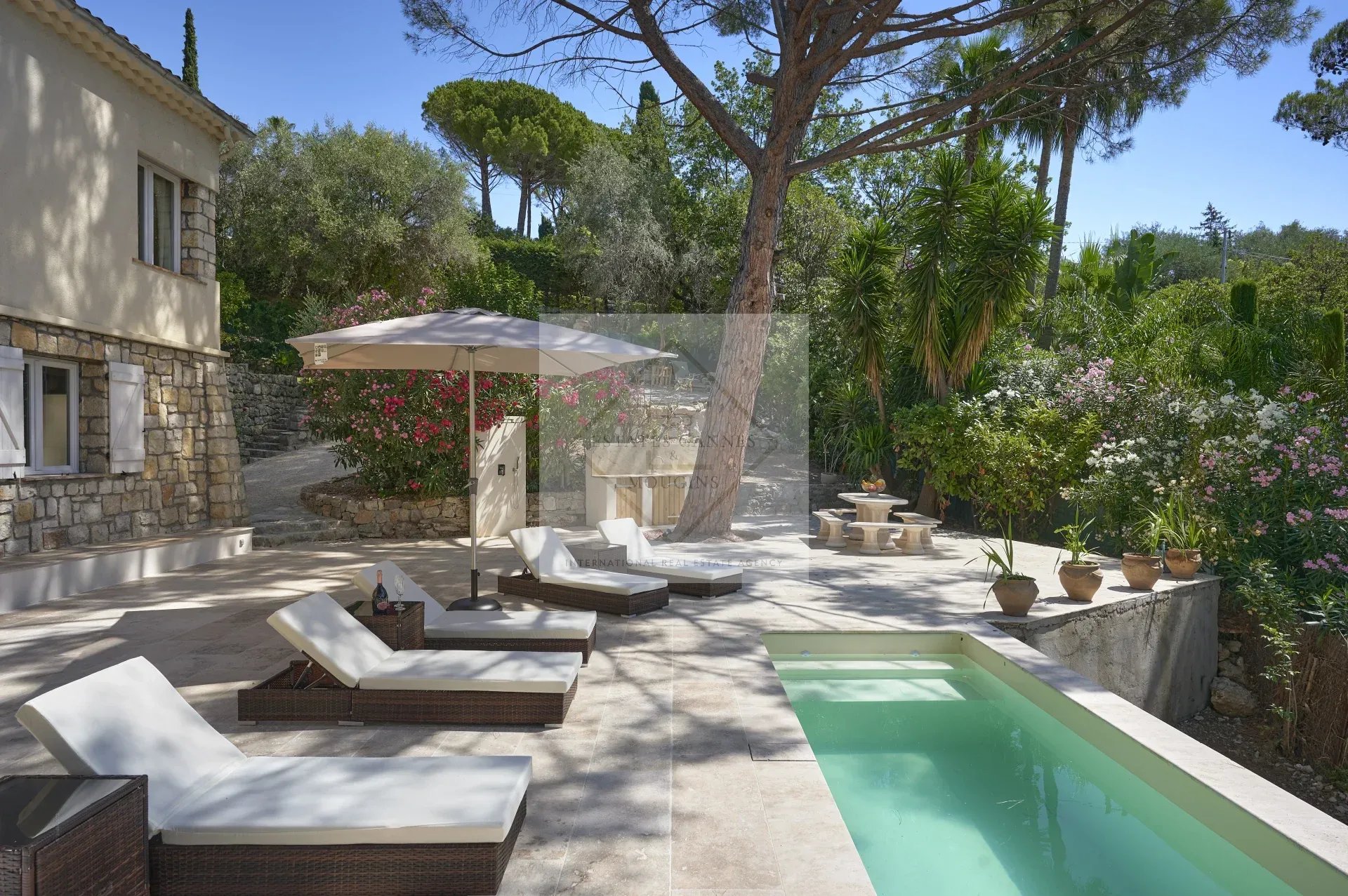 Sunny terrace with sun loungers and swimming pool in Mougins, surrounded by greenery and flowers.