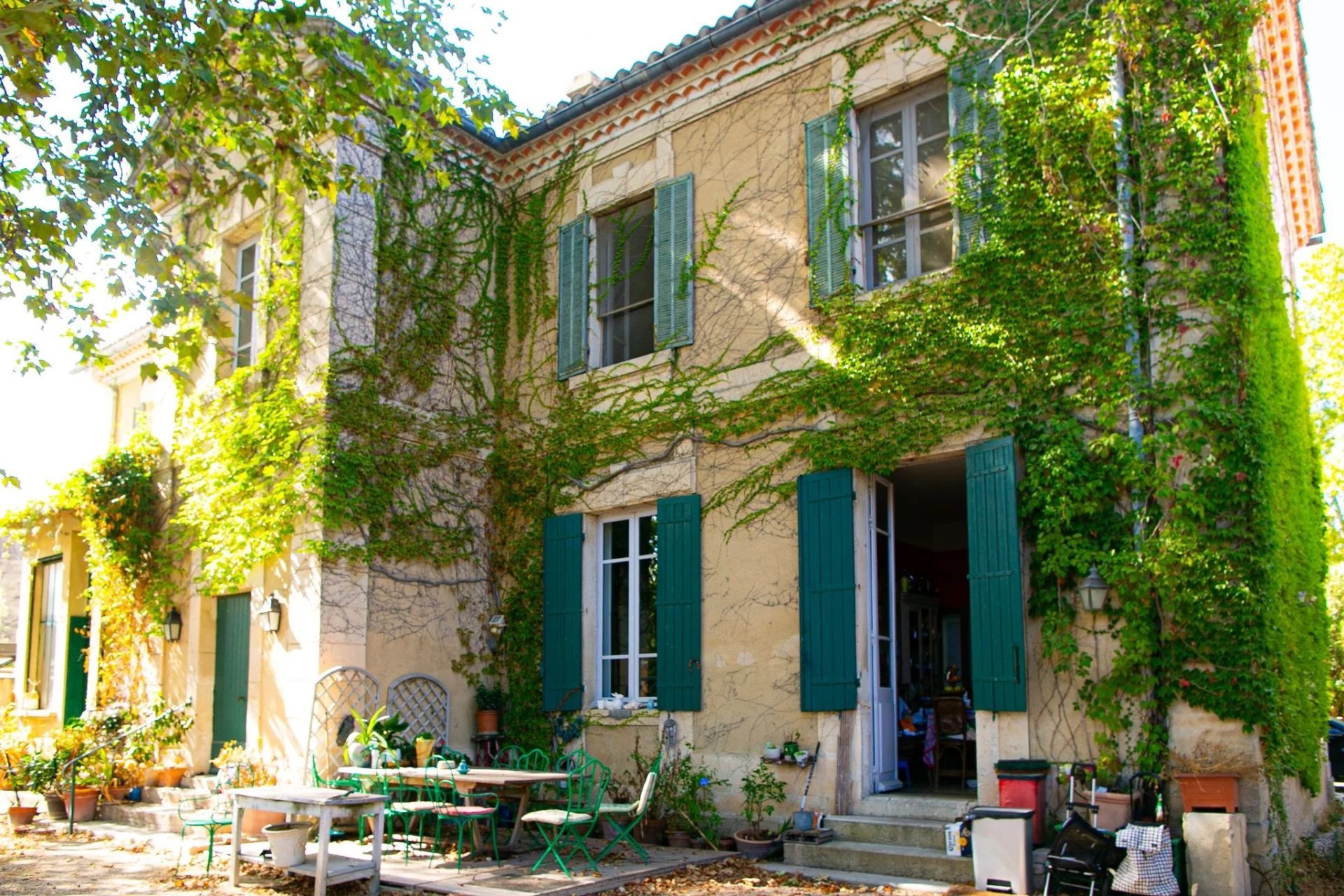 Two-story beige house covered in green ivy with teal shutters and an outdoor seating area in front.