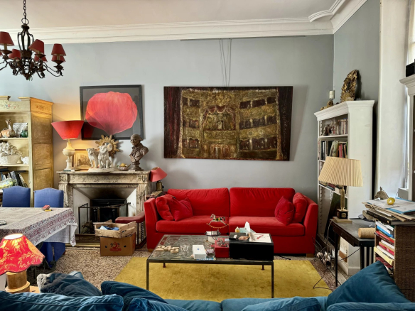Eclectic living room with a bright red sofa, yellow rug, and a glass coffee table topped with books and decorations.