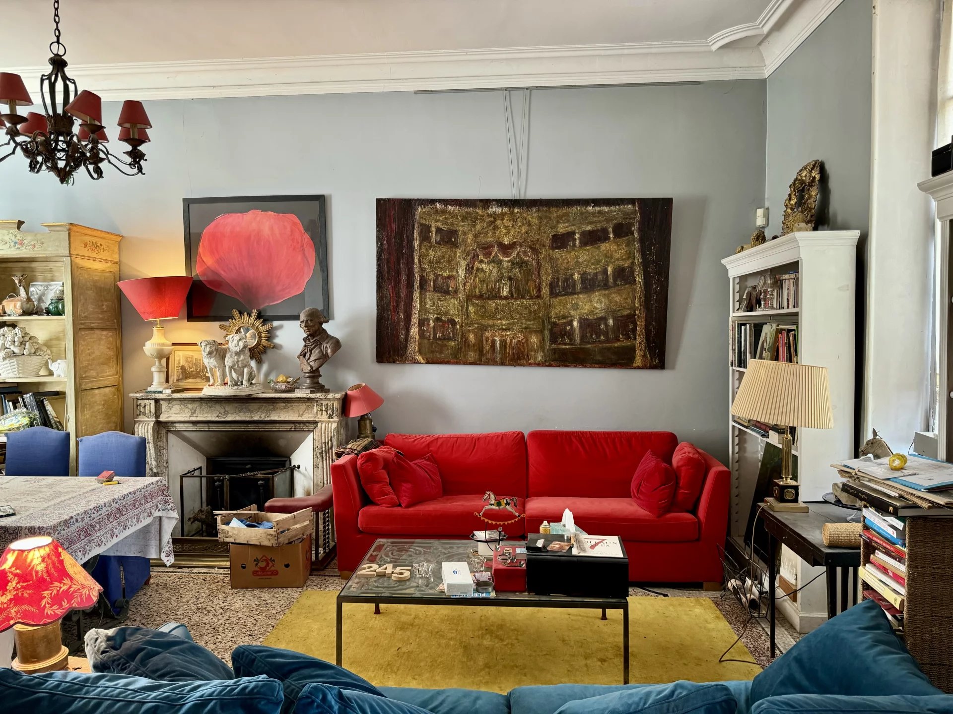 Eclectic living room with a bright red sofa, yellow rug, and a glass coffee table topped with books and decorations.