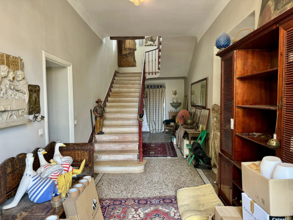 A cluttered vintage foyer with a staircase, statues, and assorted decor along both walls and a wooden cabinet on the right.
