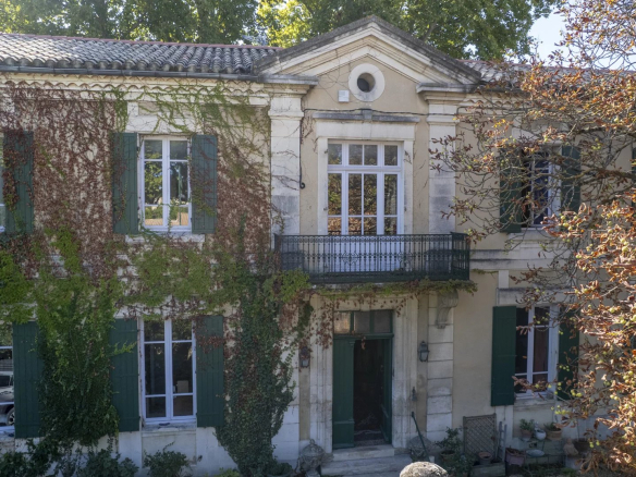Beige two-story house with green shutters, ivy covering the walls, and a small balcony above the entrance.
