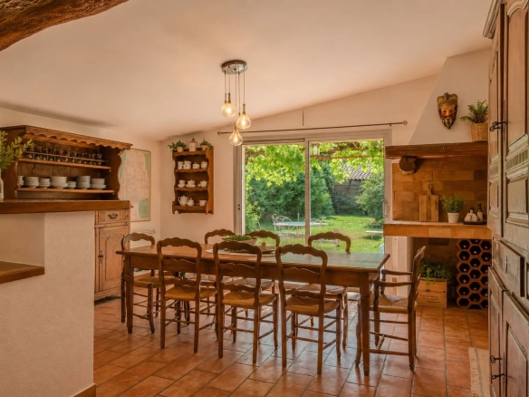 Intérieur d'une salle à manger avec une grande table en bois et une vue sur le jardin.