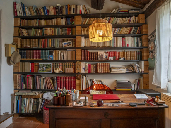 Intérieur d'un bureau avec étagères remplies de livres et un bureau en bois, éclairé par une lampe suspendue.