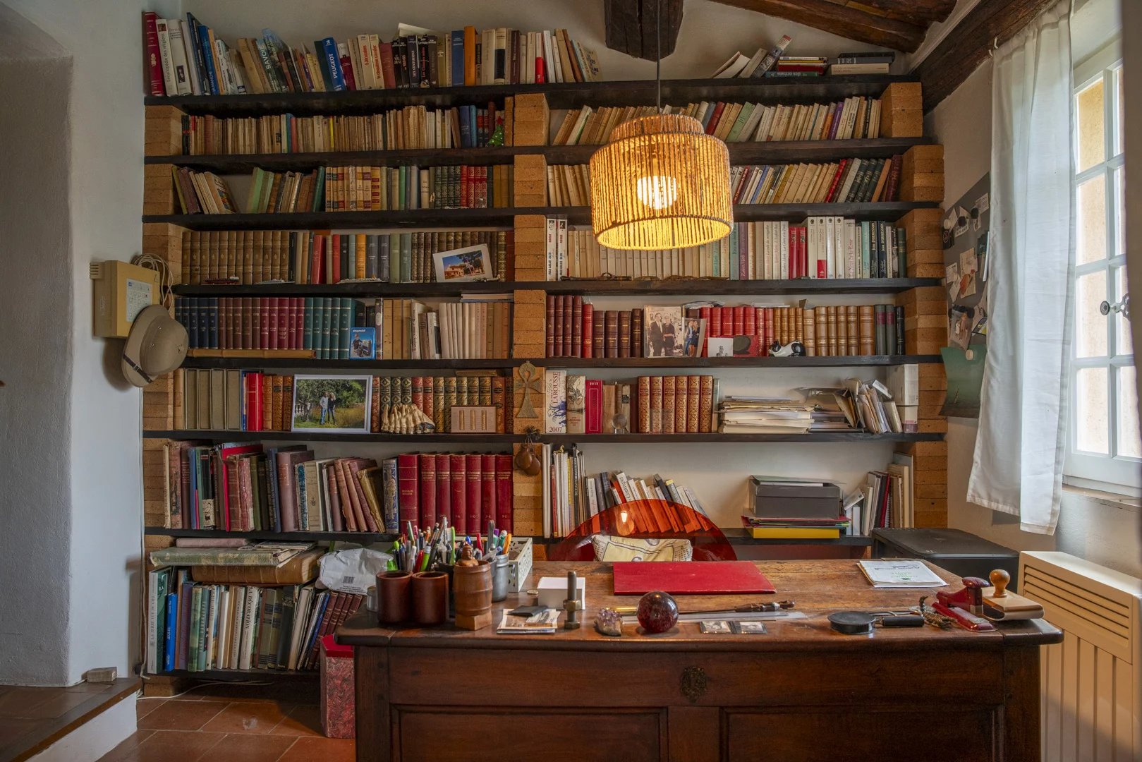 Intérieur d'un bureau avec étagères remplies de livres et un bureau en bois, éclairé par une lampe suspendue.