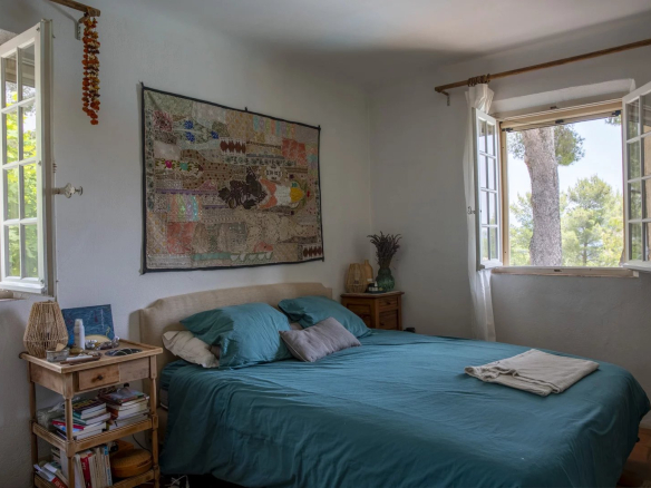 Chambre avec lit double, fenêtres ouvertes sur la verdure, décor méditerranéen.
