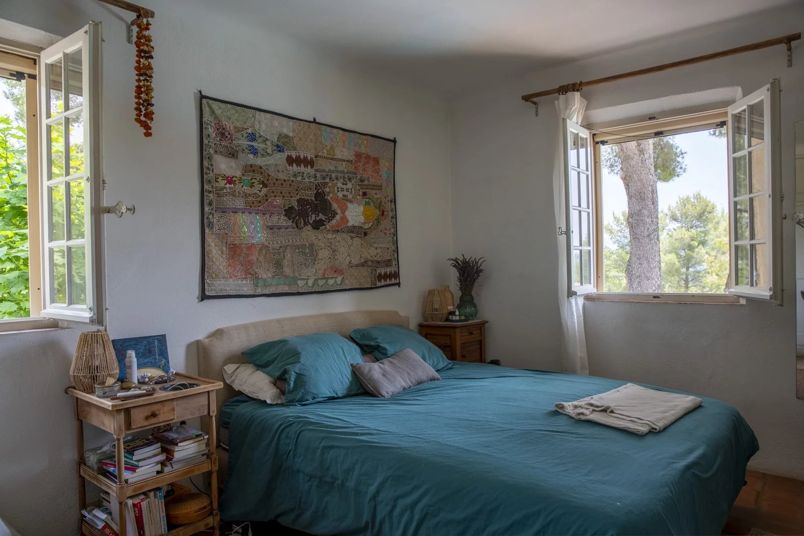 Chambre avec lit double, fenêtres ouvertes sur la verdure, décor méditerranéen.