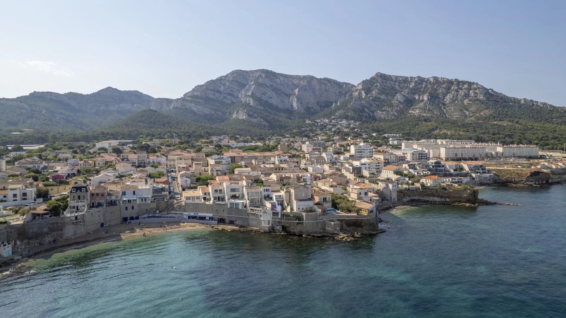 Vue côtière de Marseille Vue aérienne de la côte méditerranéenne avec des maisons en bord de mer et des montagnes en arrière-plan.