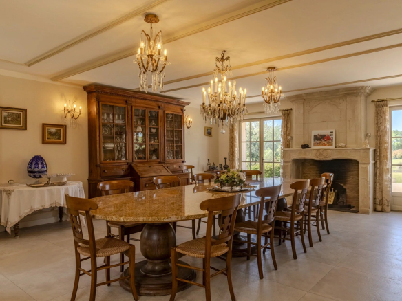 Salle à manger d'une propriété élégante avec table ronde en marbre et lustres, vue sur le jardin.