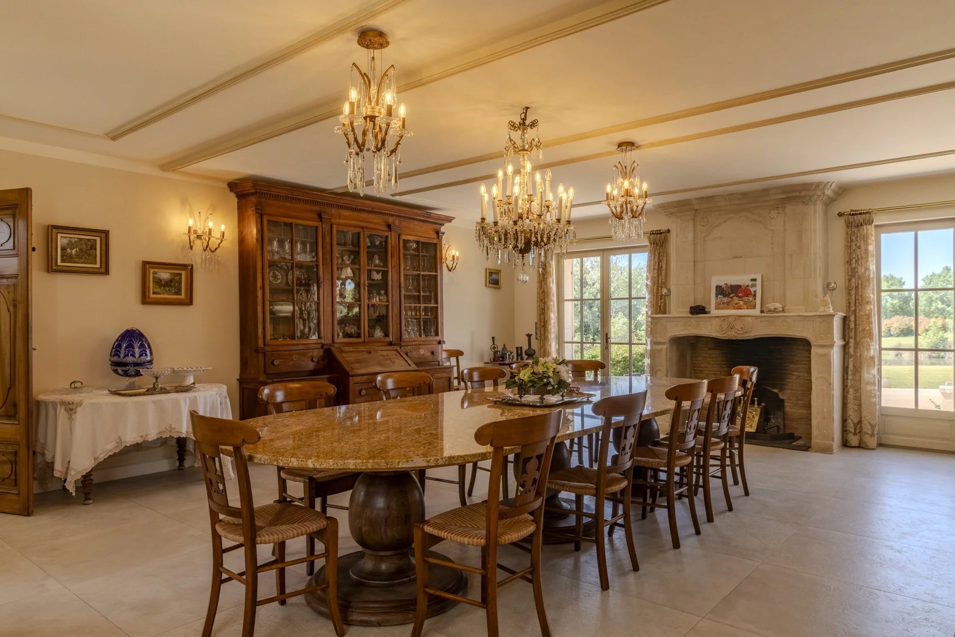 Salle à manger d'une propriété élégante avec table ronde en marbre et lustres, vue sur le jardin.