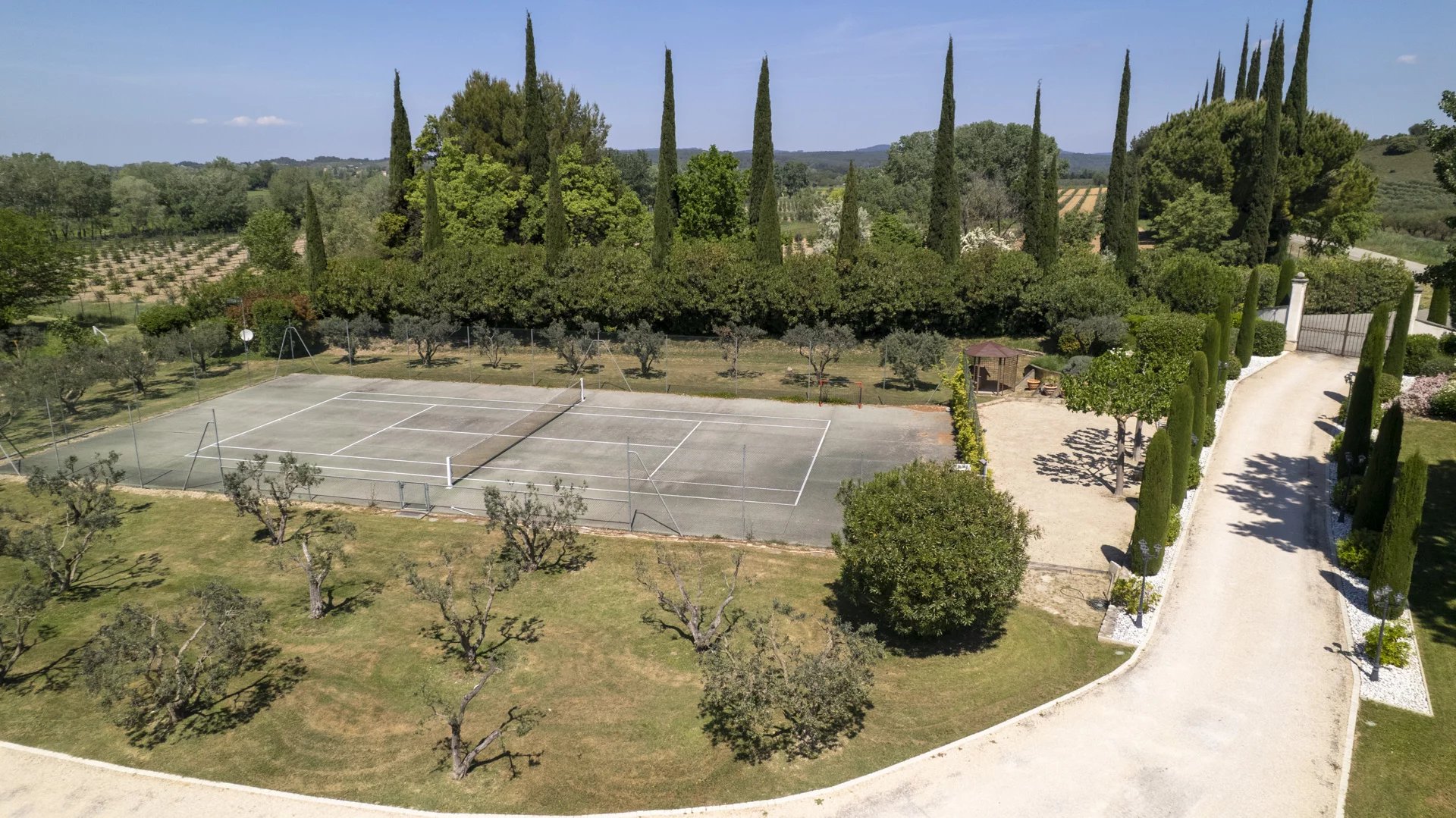 Vue aérienne d'un terrain de tennis entouré d'arbres et d'un parc paysager à Raphèle-lès-Arles.