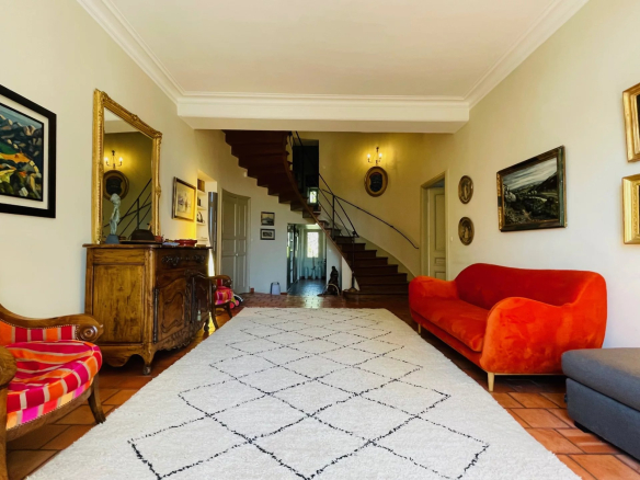 Interior of a Provençal country house with a large living room, a wooden staircase and antique furniture.