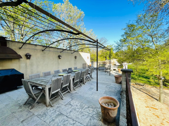 Terrace of a Provençal country house with wooden table and chairs, surrounded by trees.