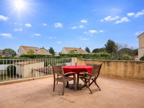 Terrasse d'une villa à Saint-Cyr-sur-Mer avec table et chaises, ciel bleu et maisons en arrière-plan.