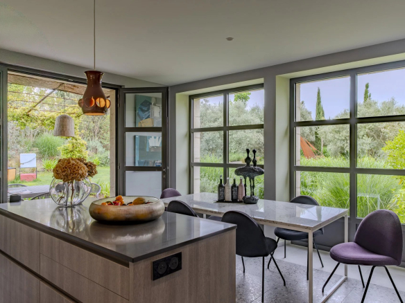 Intérieur moderne d'une cuisine avec table à manger et grandes fenêtres donnant sur le jardin.