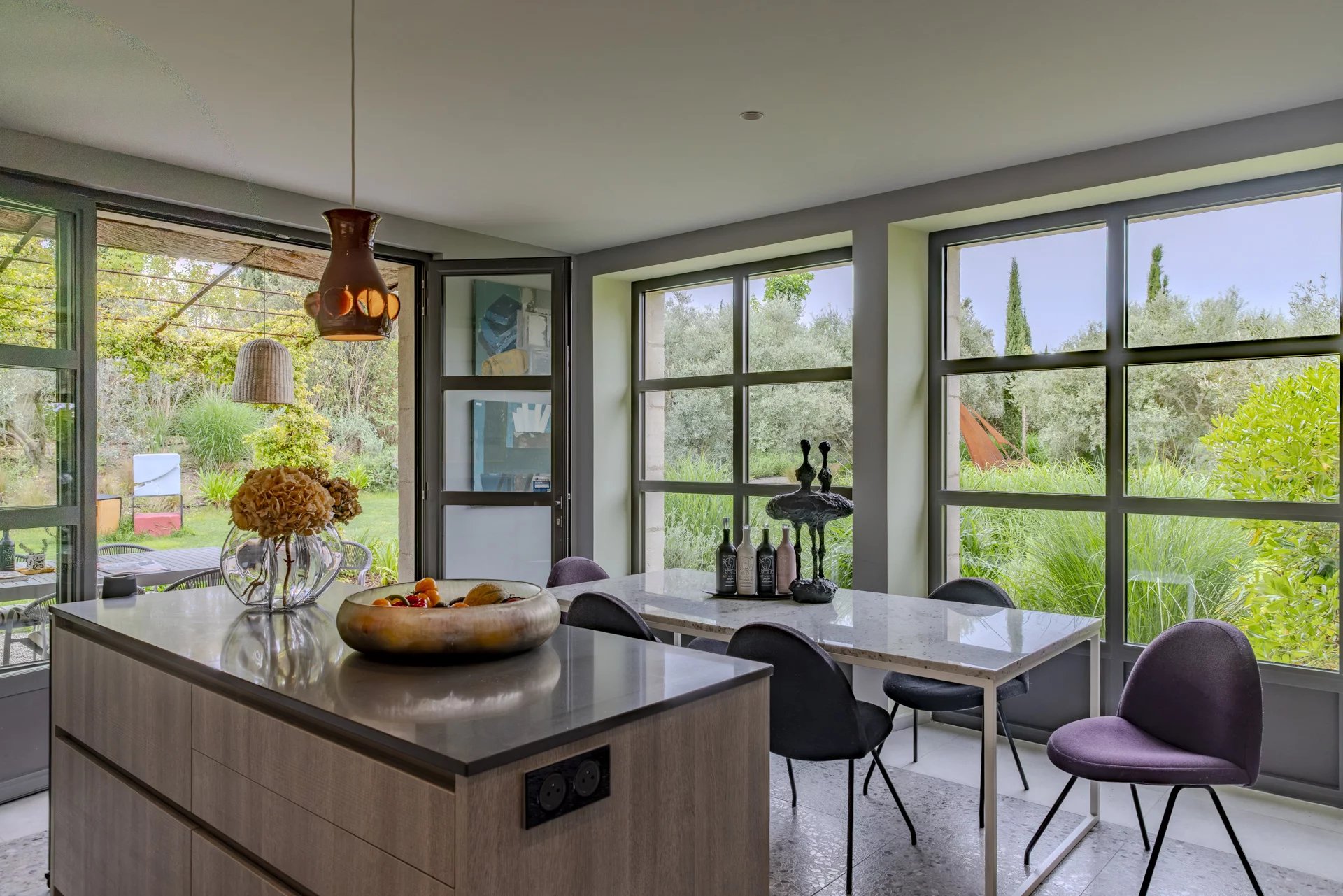 Cuisine contemporaine avec vue sur le jardin Intérieur moderne d'une cuisine avec table à manger et grandes fenêtres donnant sur le jardin.