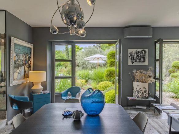 Intérieur d'une maison moderne avec vue sur un jardin, table à manger, et décor contemporain.