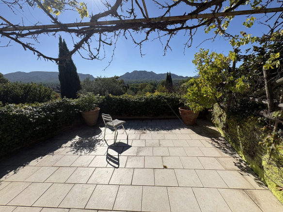 Terrasse d'une maison en pierre avec vue sur les Alpilles, entourée de végétation méditerranéenne.