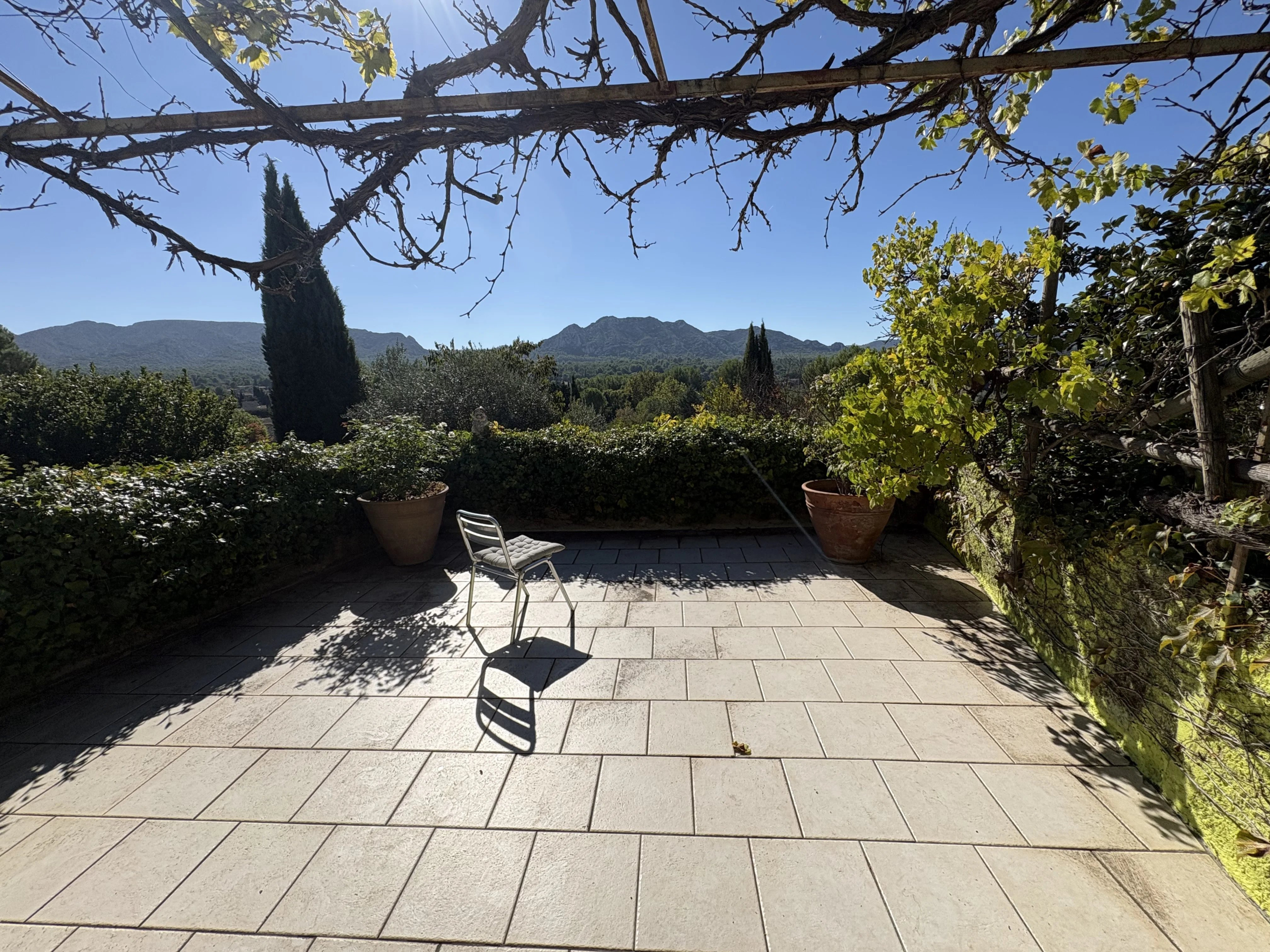 Terrasse avec vue sur les Alpilles Terrasse d'une maison en pierre avec vue sur les Alpilles, entourée de végétation méditerranéenne.