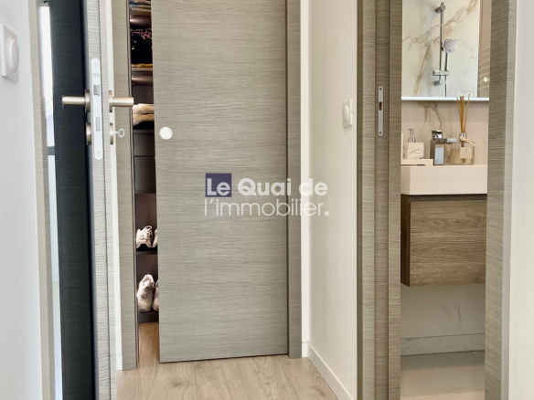 Contemporary hallway view: gray door ajar shows a stacked closet with folded clothes; a nearby doorway reveals a marble-bench bathroom vanity.