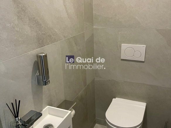 Modern grey-tiled bathroom with a wall-mounted toilet and a small white wall sink with chrome faucet.