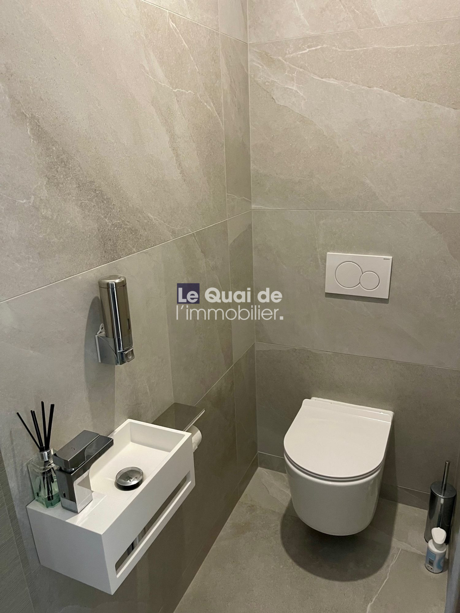 Modern grey-tiled bathroom with a wall-mounted toilet and a small white wall sink with chrome faucet.